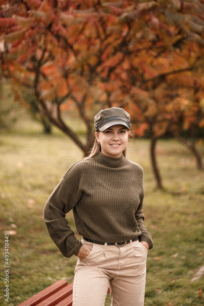 Beautiful blonde Ukrainian woman in a green knitted sweater and light jeans in an autumn park with orange trees. Golden autumn Beautiful blonde Ukrainian woman in a green knitted sweater and light jeans in an autumn park with orange trees. Golden autumn
