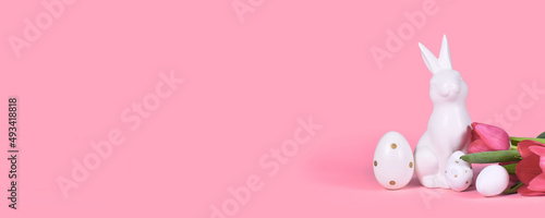 Banner with easter bunny, white eggs with golden dots and tulip spring flowers on pink background with copy space