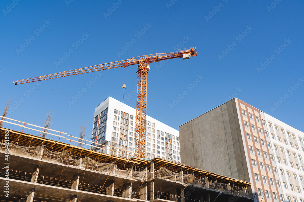 A crane builds a house, a yellow hoist participates in the construction of a residential building, lifting heavy loads to a height.