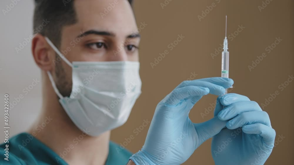 Hispanic man doctor medical surgeon wear medical face mask gloves pressing filled syringe tapping medicine bubbles liquid preparing inject vaccine anesthesia for surgery medicine treatment concept Hispanic man doctor medical surgeon wear medical face mask gloves pressing filled syringe tapping medicine bubbles liquid preparing inject vaccine anesthesia for surgery medicine treatment concept