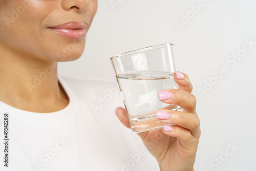 Healthy and hydrated. Side view of young african american woman drinking pure mineral water while standing isolated over grey studio background. Maintenance of fluid balance and hydration concept