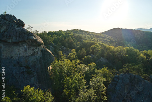 Aerial view of bright landscape with green forest trees and big rocky boulders between dense woods in summer. Beautiful scenery of wild woodland