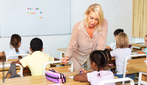 Positive woman teacher helping preteen schoolchildren during lesson in schoolroom