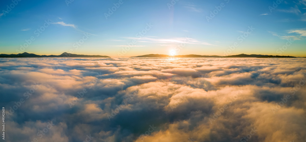 Aerial view of yellow sunset over white puffy clouds with distant mountains on horizon