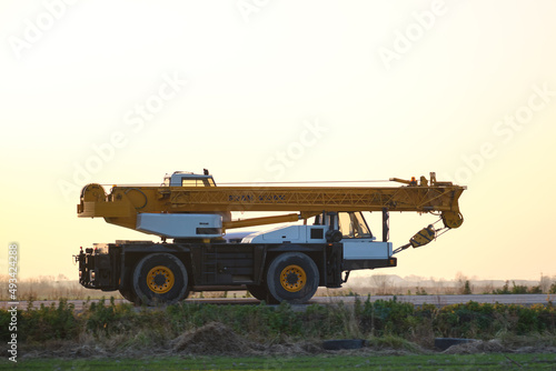 Heavy duty mobile lifting crane driving on intercity road at sunset