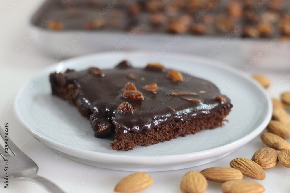 Slice of Texas sheet cake served on a plate. Buttery and chocolaty cake sliced to rectangular pieces inside the baking bin and scooped from it Slice of Texas sheet cake served on a plate. Buttery and chocolaty cake sliced to rectangular pieces inside the baking bin and scooped from it