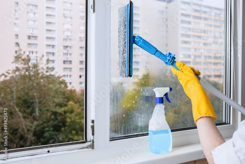 Man in yellow rubber gloves cleaning window with cleaner spray detergent and squeegee or rag at home or office, copy space. Housework and housekeeping, home hygiene photo