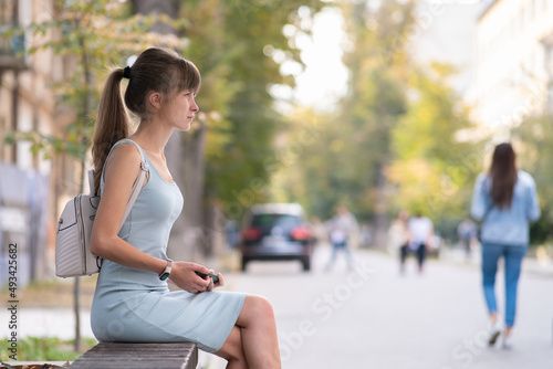 Young woman sitting alone on city street outdoors waiting for someone to arrive. Arriving late on business meeting concept