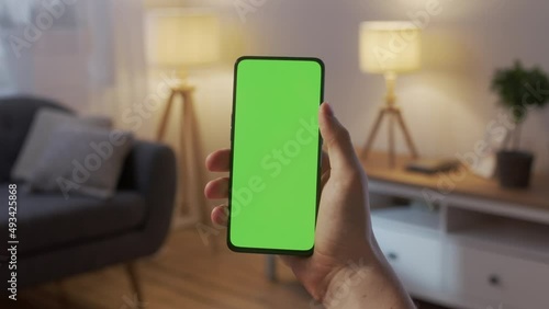 Handheld Camera: Point of View of Young Man at Home Sitting on Living Room at Night With Green Mock-up Screen Smartphone. Boy is Watcing Content Without Touching Gadget Screen. Modent Technology photo