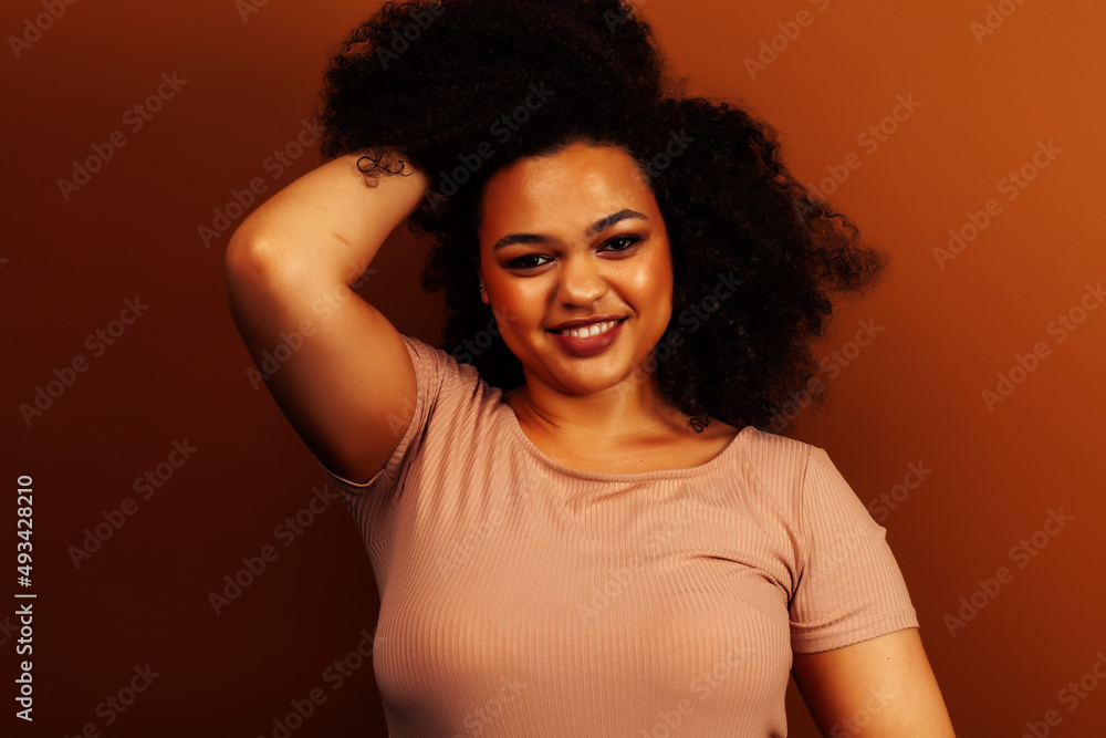 pretty young african american woman with curly hair posing cheerful gesturing on brown background, lifestyle people concept pretty young african american woman with curly hair posing cheerful gesturing on brown background, lifestyle people concept