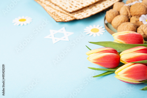 Passover greeting card with matzah, nuts, tulip and daisy flowers on blue background.