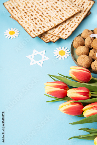 Passover greeting card with matzah, nuts, daisy and tulip flowers on blue background.