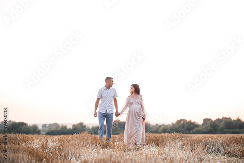 A young pregnant woman with her husband  a happy beautiful couple hugging on a golden field in the countryside. Family relationships. Future parents