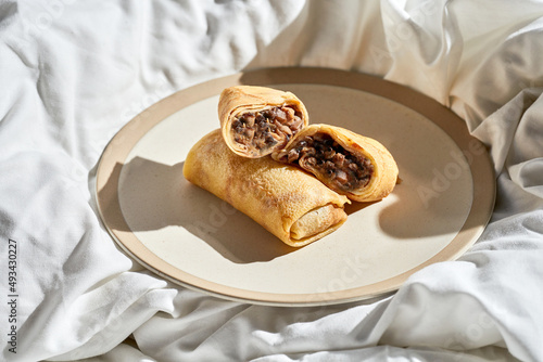Chicken and mushroom crepes in a plate on a white sheet. Hard light.