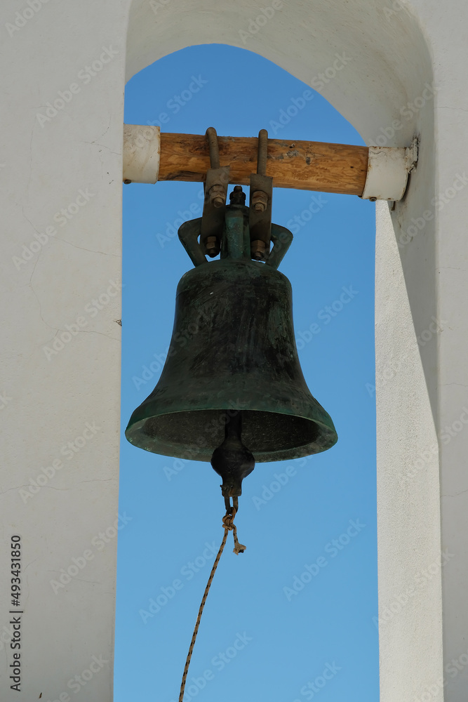 Obraz premium Closeup of a traditional church bell hanging from a wooden pilar and the aegean sea in the background in Santorini
