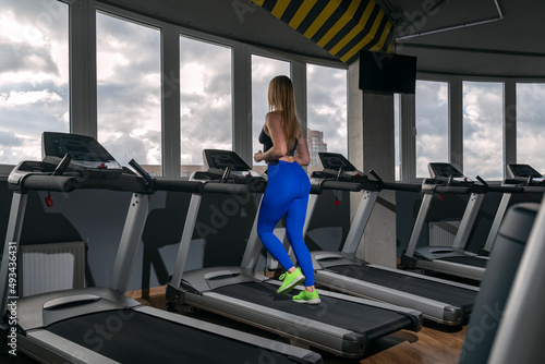 Sports blonde girl running on the treadmill in the empty modern gym. Cardio workout on running track