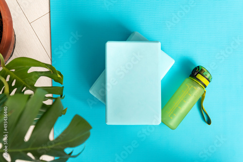 Top view of bluey yoga mat, bottle with water, yoga bricks and green plant. Workout at home. Fitness Equipment. Top view. photo