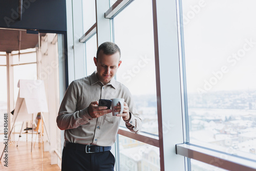 Male brokers with phone looking towards window with coffee in hand in modern workspace