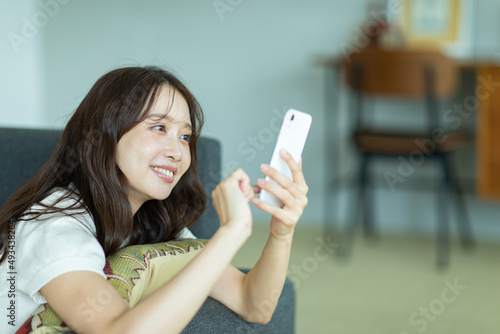 ソファに寝転んでスマートフォンを操作する女性 photo
