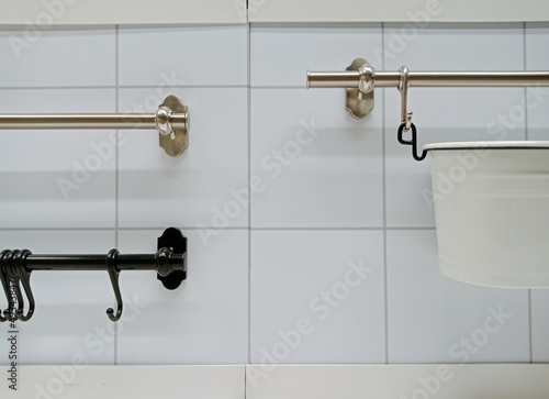 Stainless hangers and hooks on white tile wall. Kitchenware hanging on white wall.