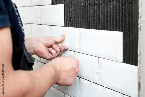 The master's hands press a white ceramic tile against the wall The stage of facing the kitchen wall with white ceramic tiles. Construction details, repair work photo