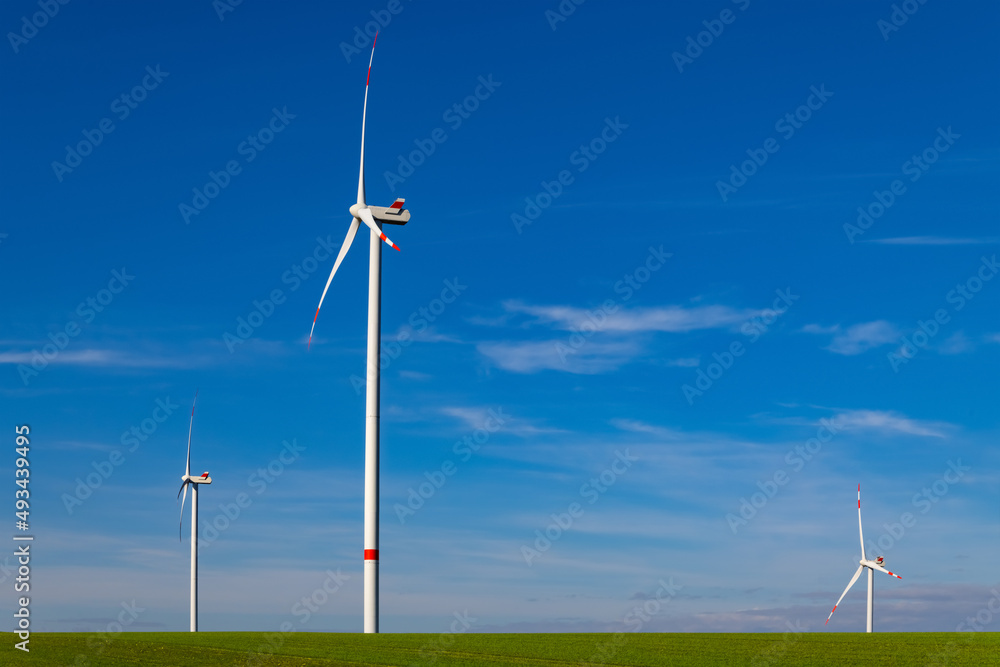 Renewable wind energy symbolized by three tall windmill turbines with blue sky on a sunny day in Germany. Sustainability through natural power generated by technological inventions and climate.