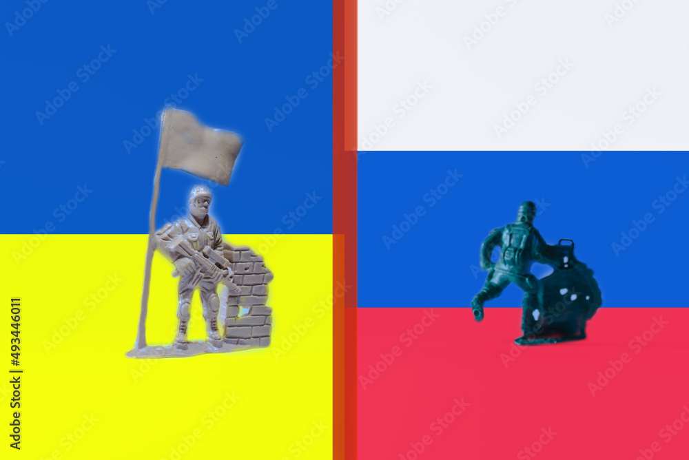 Miniature toy Ukrainian soldier holding ukraine flag a soldier running in the distance.Indoors shot,copy space.Russia and ukraine flags background. Miniature toy Ukrainian soldier holding ukraine flag a soldier running in the distance.Indoors shot,copy space.Russia and ukraine flags background.