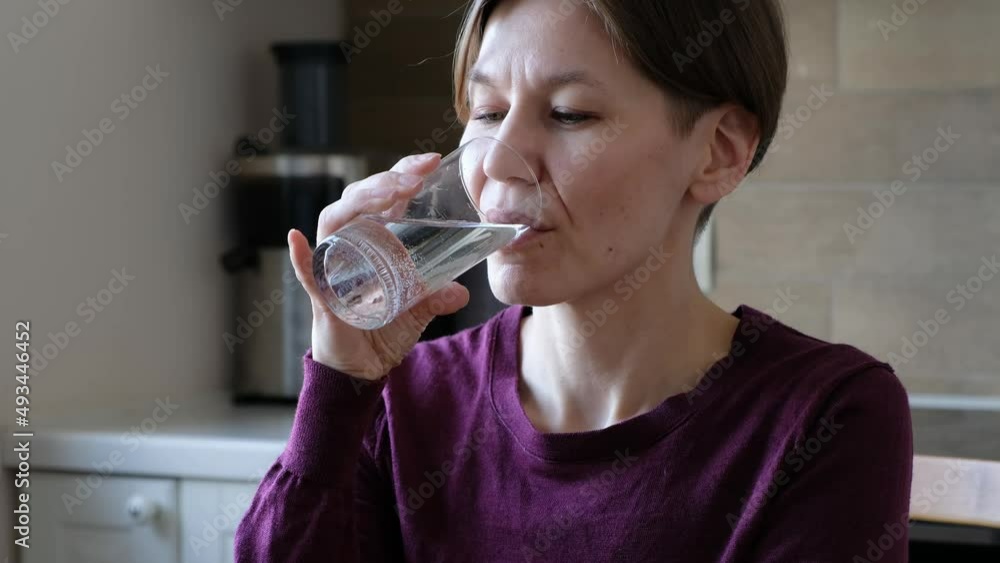 Woman Taking a Pill and Drinking a Glass of Water in the kitchen Woman Taking a Pill and Drinking a Glass of Water in the kitchen