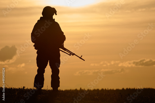 Military soldier silhouette with machine gun over sunset