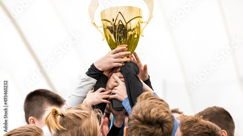 Happy kids winning sports tournament. Schoolboys standing in a circle and holding the golden trophy. Victory celebration of a youth sports team
