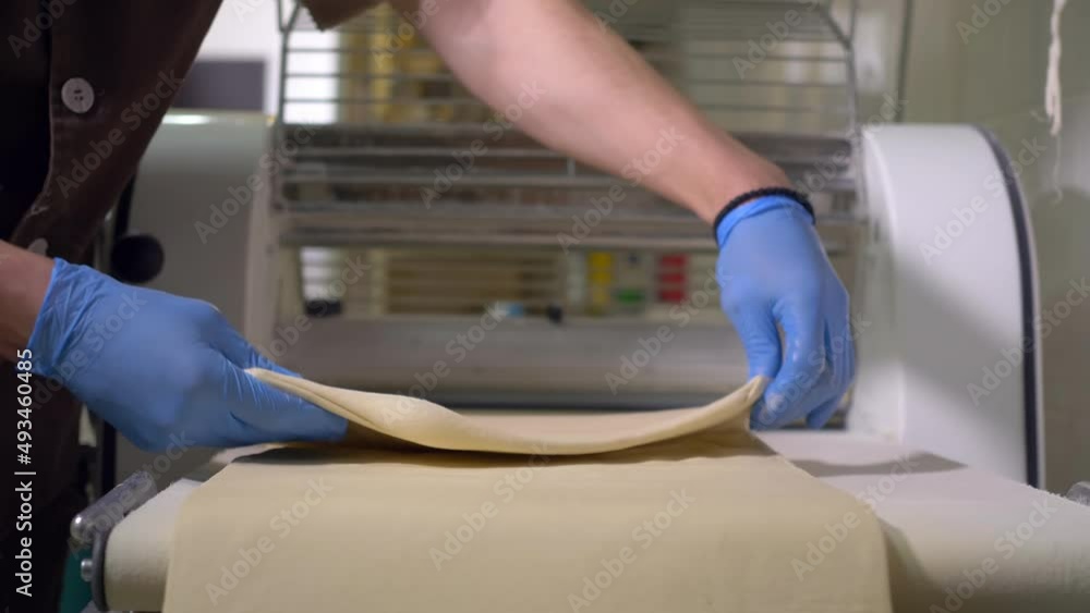 Baker rolls dough on a dough sheeter to make pizza and pane in a bakery factory Baker rolls dough on a dough sheeter to make pizza and pane in a bakery factory