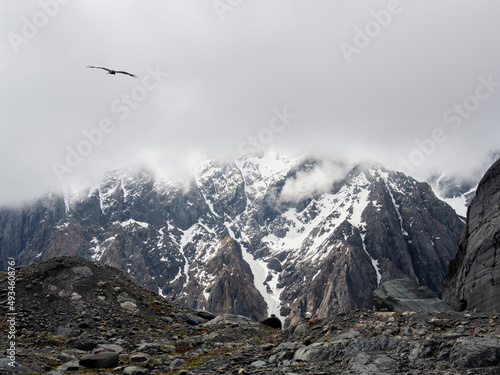 Atmospheric ghostly landscape with fuzzy silhouettes of snow rocks in low clouds. Dramatic view to large mountains blurred in rain haze in gray low clouds. Sharp cliff of the mountain.