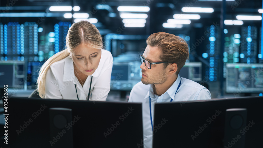 IT Specialist Works on Two Personal Computer at the Software Program with Coding Language Interface. In the Background Technical Room of Data Center with Professional Working IT Specialist Works on Two Personal Computer at the Software Program with Coding Language Interface. In the Background Technical Room of Data Center with Professional Working