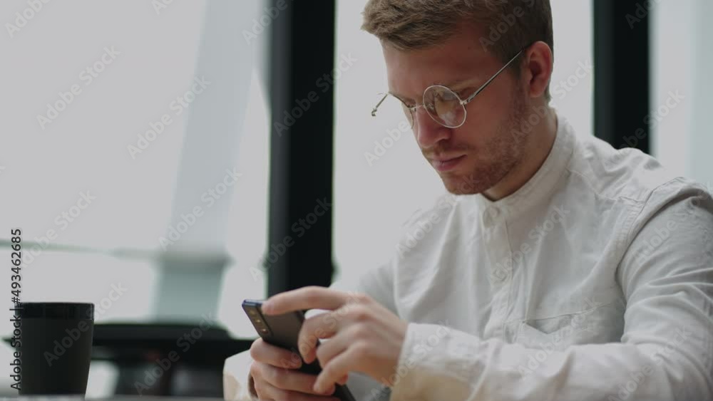 Adult businessman texting on smartphone while sitting by laptop Adult businessman texting on smartphone while sitting by laptop