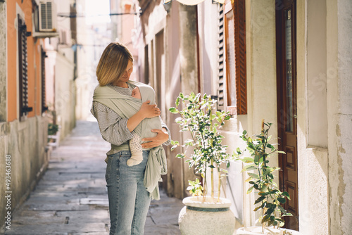 Babywearing. Mother and baby walking in town. Baby in wrap carrier. Young woman carrying little child in baby sling in mint color. Concept of green parenting, natural motherhood, postpartum period. photo