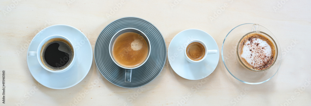 Fototapeta premium Four cups with various coffee, espresso, cappuccino, lungo, black and with crema on a light wooden table, panoramic format, copy space, high angle view from above