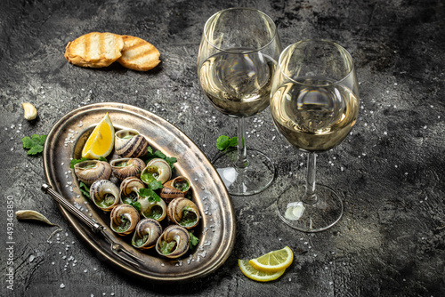 Fototapeta Naklejka Na Ścianę i Meble -  Escargots de Bourgogne or Snails with herbs, butter, garlic on metal plate with forks. wine glass. gourmet food. Restaurant menu, dieting, cookbook recipe