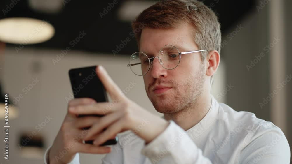 Attractive man Glasses standing alone indoor holding in hands smart phone dial number on touchscreen. Cheerful young female surfing internet, web surfing website, choose buying goods on-line concept Attractive man Glasses standing alone indoor holding in hands smart phone dial number on touchscreen. Cheerful young female surfing internet, web surfing website, choose buying goods on-line concept