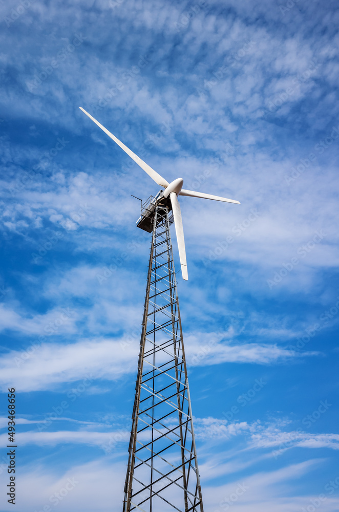 Wind turbine on a metal truss tower, against the background of a blue sky with clouds. Photo taken in Russia