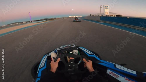 Point of view man driving a kart outdoor at sunset. Racers driving karts on a race track. First person view of steering a go cart while racing in a fun competition photo