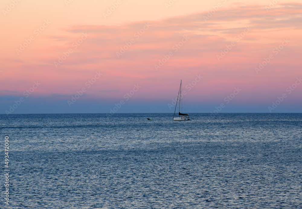 Fototapeta premium Sailboat at sea on sailing on the waves. Yachtsman during training on a sailboat. Skiff and Sailboat in sea port near the Spanish coast. Sail sport in Yacht club. Sail boat on waves on sunset in sea.