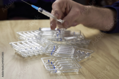 a man puts ampoules with medicines on the table and a syringe in his hand