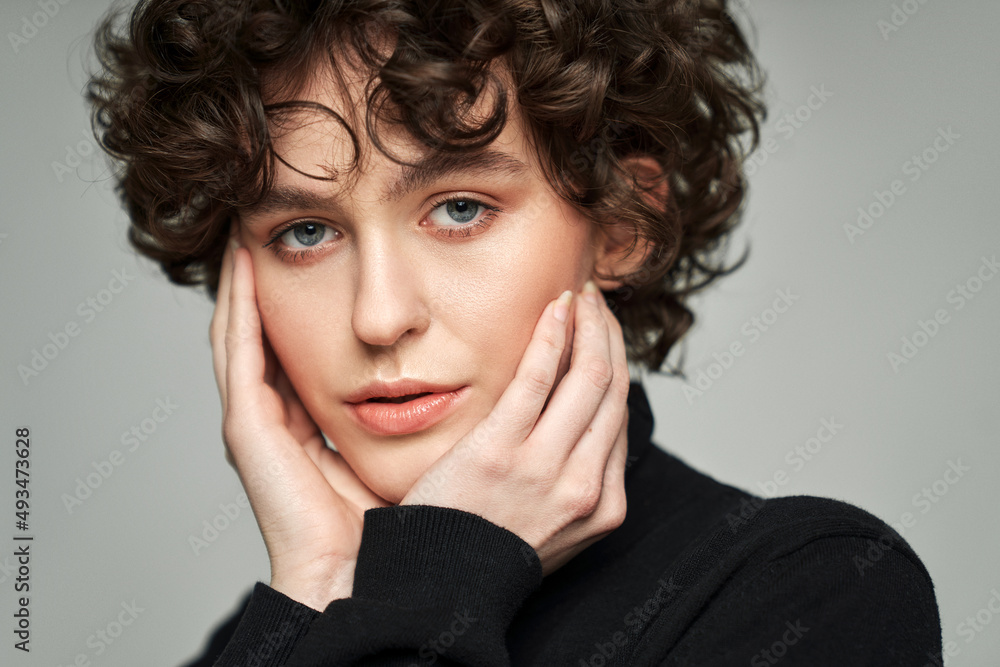 Portrait of brunette with curls wear high neck jumper touching cheeks Portrait of brunette with curls wear high neck jumper touching cheeks