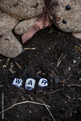 rustic style teddy bear on muddy soil with the word war written in letter dice, illustrating a childhood during a time of war photo