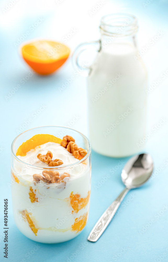 Greek yogurt with orange and walnuts in glasses on a blue table. Healthy food. Health eating concept. Selective focus. Greek yogurt with orange and walnuts in glasses on a blue table. Healthy food. Health eating concept. Selective focus.