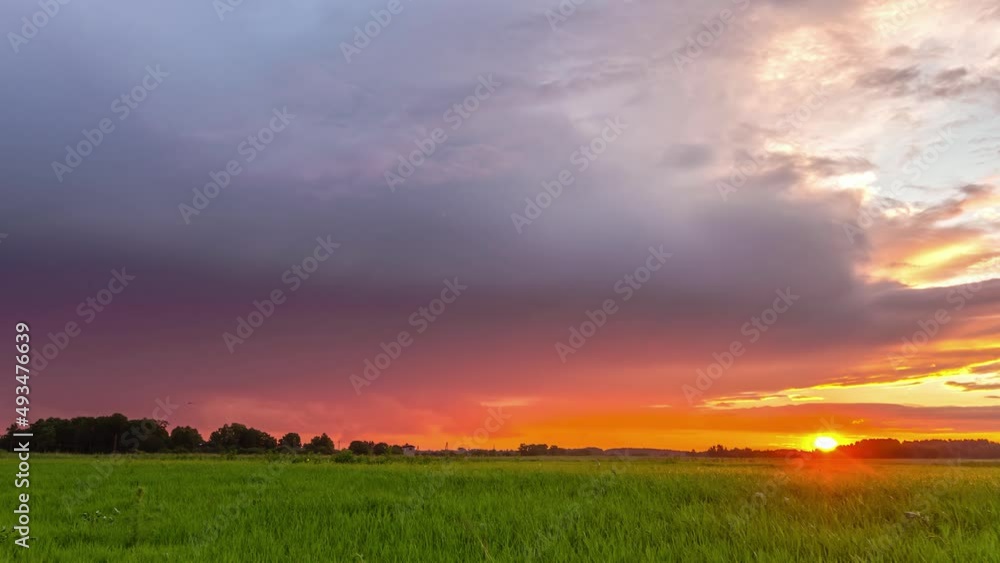 Static view of scenic setting sun over the horizon in timelapse. Dark clouds movement in the golden sky over green agricultural fields in the evening. Static view of scenic setting sun over the horizon in timelapse. Dark clouds movement in the golden sky over green agricultural fields in the evening.