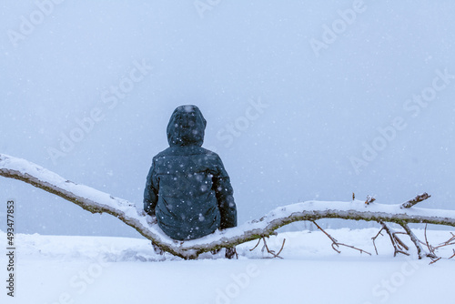 a boy sits on a tree branch and looks into the void, it is snowing