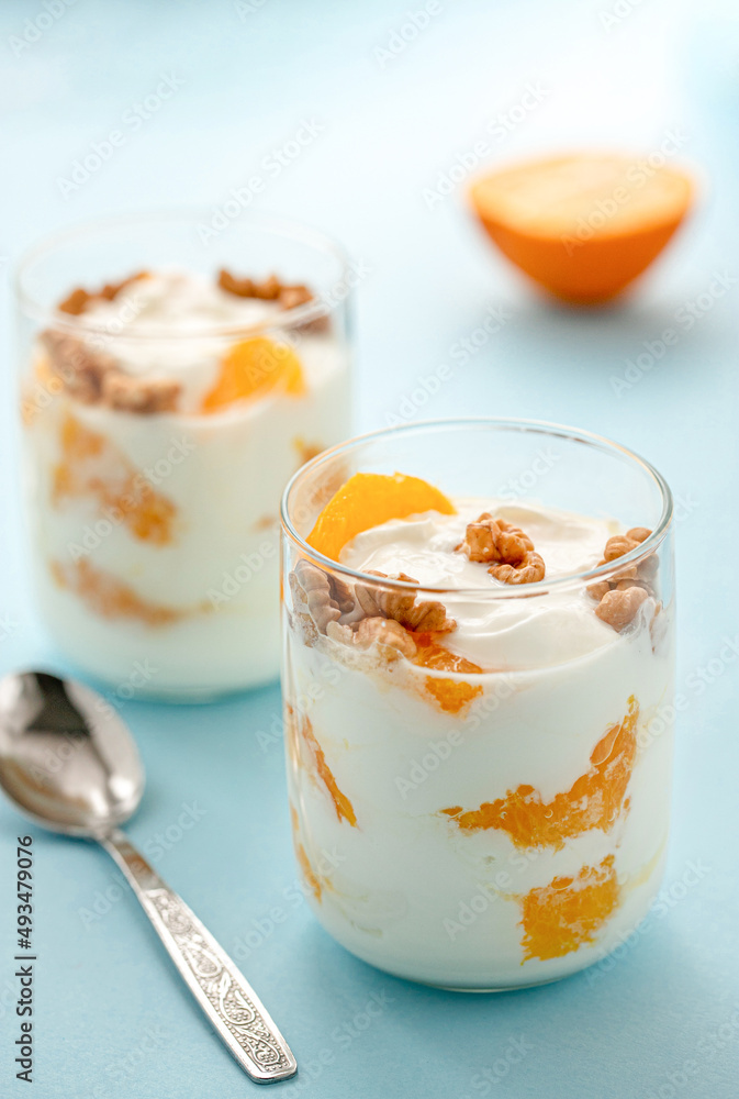 Greek yogurt with orange and walnuts in glasses on a blue table. Healthy food. Health eating concept. Selective focus.