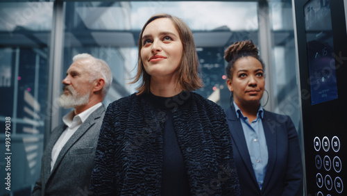 Three Diverse Multiethnic International People Ride a Glass Elevator to Office in a Modern Business Center. Focus on a Happy Young Beautiful Businesswoman Standing in Front in a Lift. © Gorodenkoff
