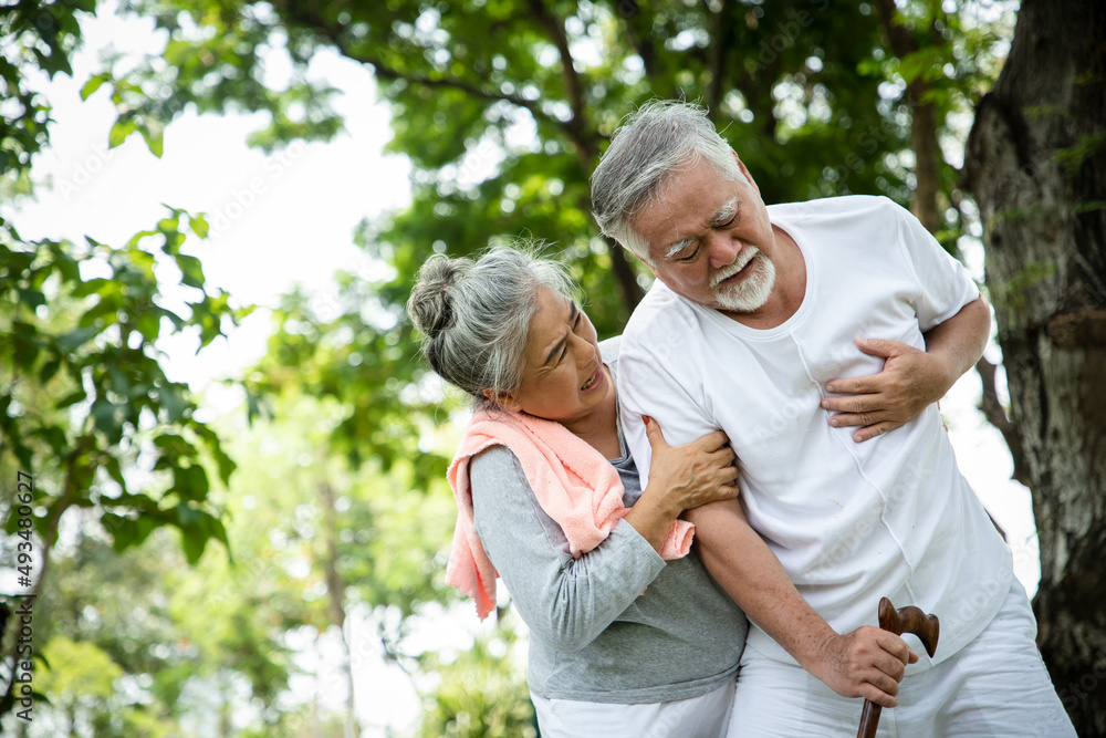 An elderly woman supports her husband from angina caused by a heart attack in her backyard while exercising. Concept of accident and life insurance An elderly woman supports her husband from angina caused by a heart attack in her backyard while exercising. Concept of accident and life insurance